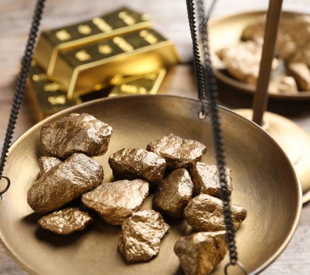 Scale pan with gold lumps on wooden table, closeup