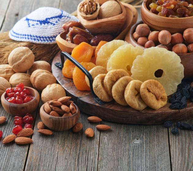 Tu Bishvat celebration concept. Mix of dry fruits and nuts almonds, hazelnuts, walnuts, apricots, prunes, cherries, raisins, dates, apples, figs over wooden table. Jewish holiday, new year of trees.